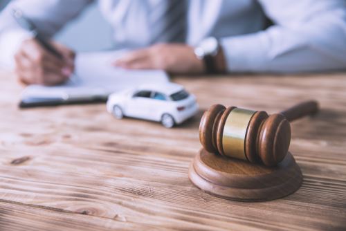 An attorney writing at a desk with a gavel and miniature car on the desk