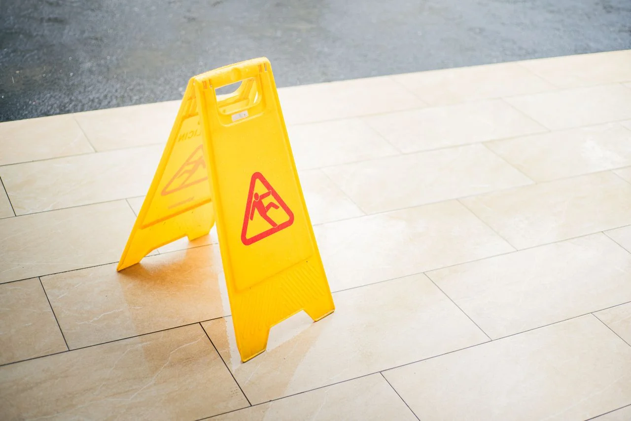 A bright yellow caution sign placed on a tile floor indicating a wet area for safety